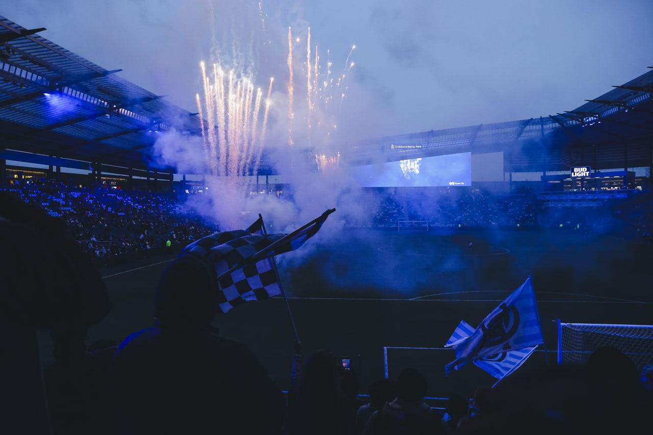 Flags are waved in the Cauldron as the pregame fireworks shoot upwards from the field.