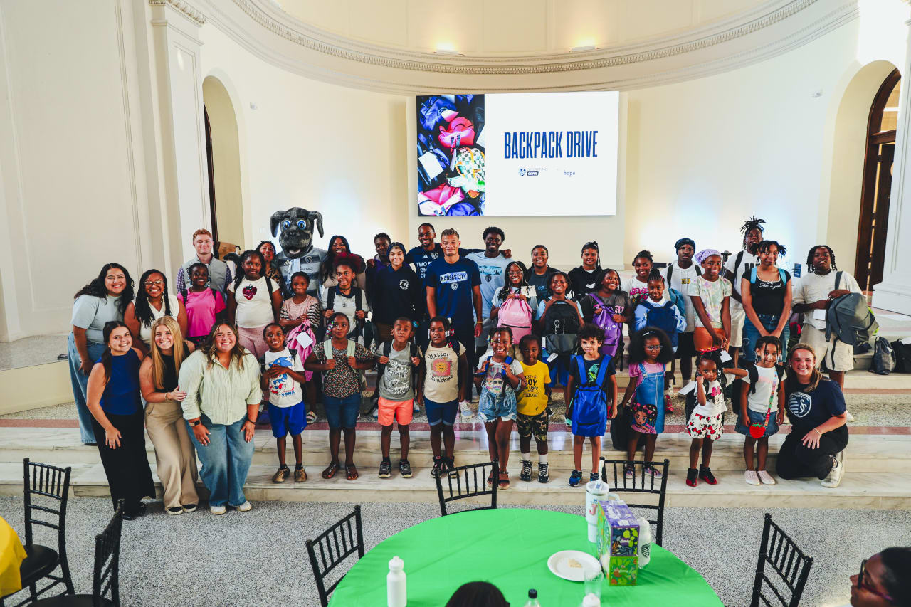 Sporting KC Mascot Blue and Sporting KC players Mason Toye, Zorhan Bassong and Stephen Afrifa, Sporting KC Staff, Hope Center staff and students all smile for a photo with a student.