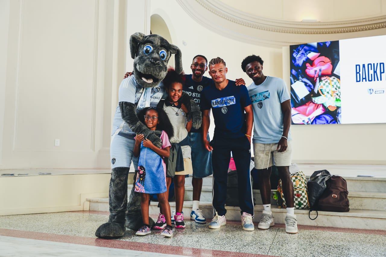 Sporting KC Mascot Blue and Sporting KC players Mason Toye, Zorhan Bassong and Stephen Afrifa smile for a photo with a student.