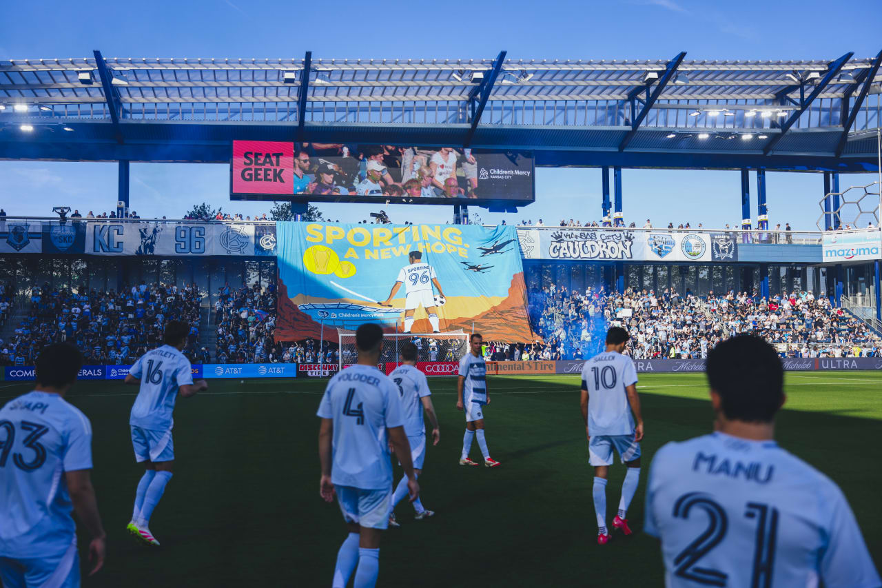 Sporting KC players walk onto the field with the tifo in the background.